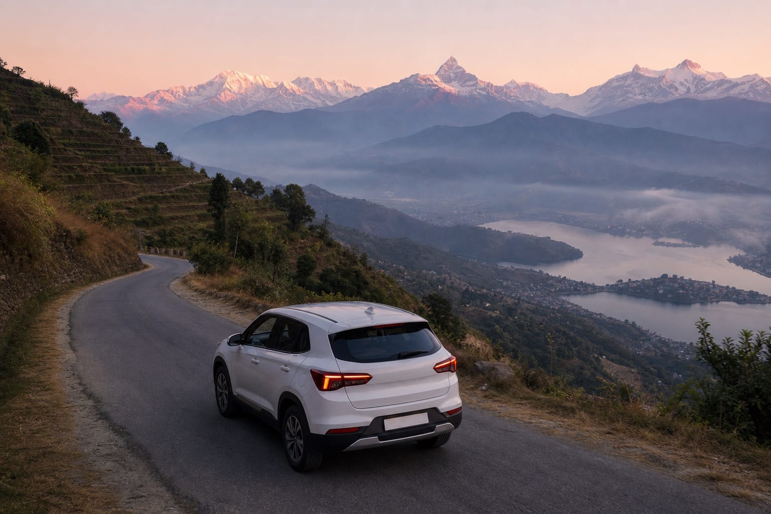 White SUV climbing the Sarangkot road at dawn above Phewa Lake, with the Annapurna range on the skyline