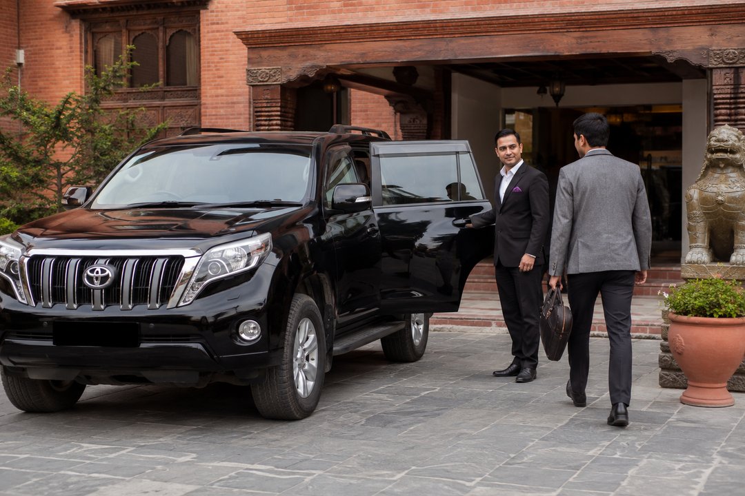 A chauffeur opening a car door for a guest at a Kathmandu hotel